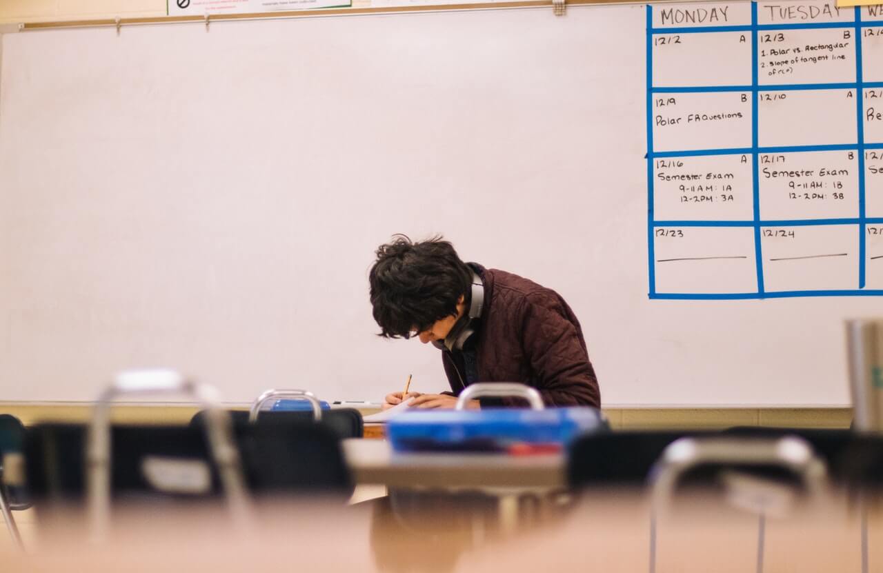 Man writing on a table in a meeting room with a schedule drawn out behind him