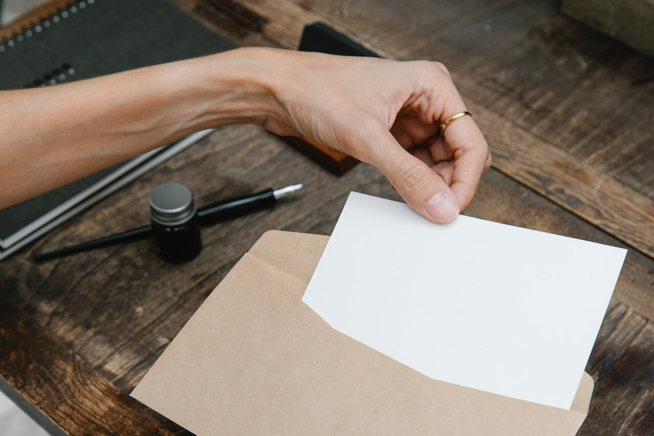 Hand slipping a white paper into a brown envelope