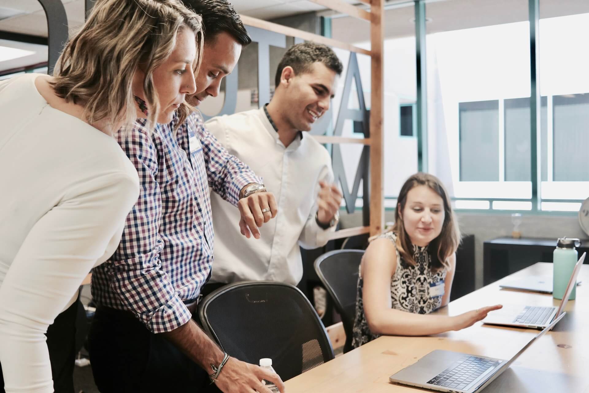 Woman sitting at an office desk with her colleagues standing behind her