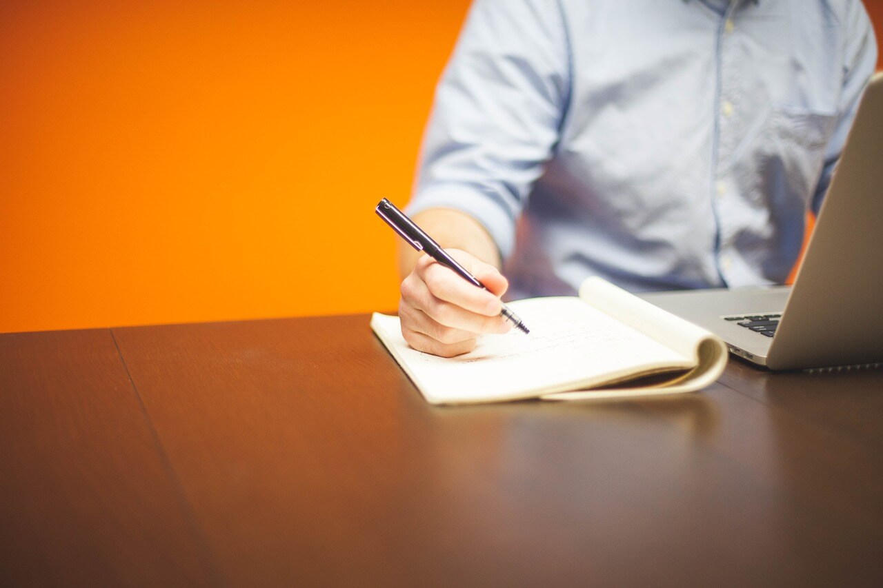 A man using a laptop and a notepad to make business plans