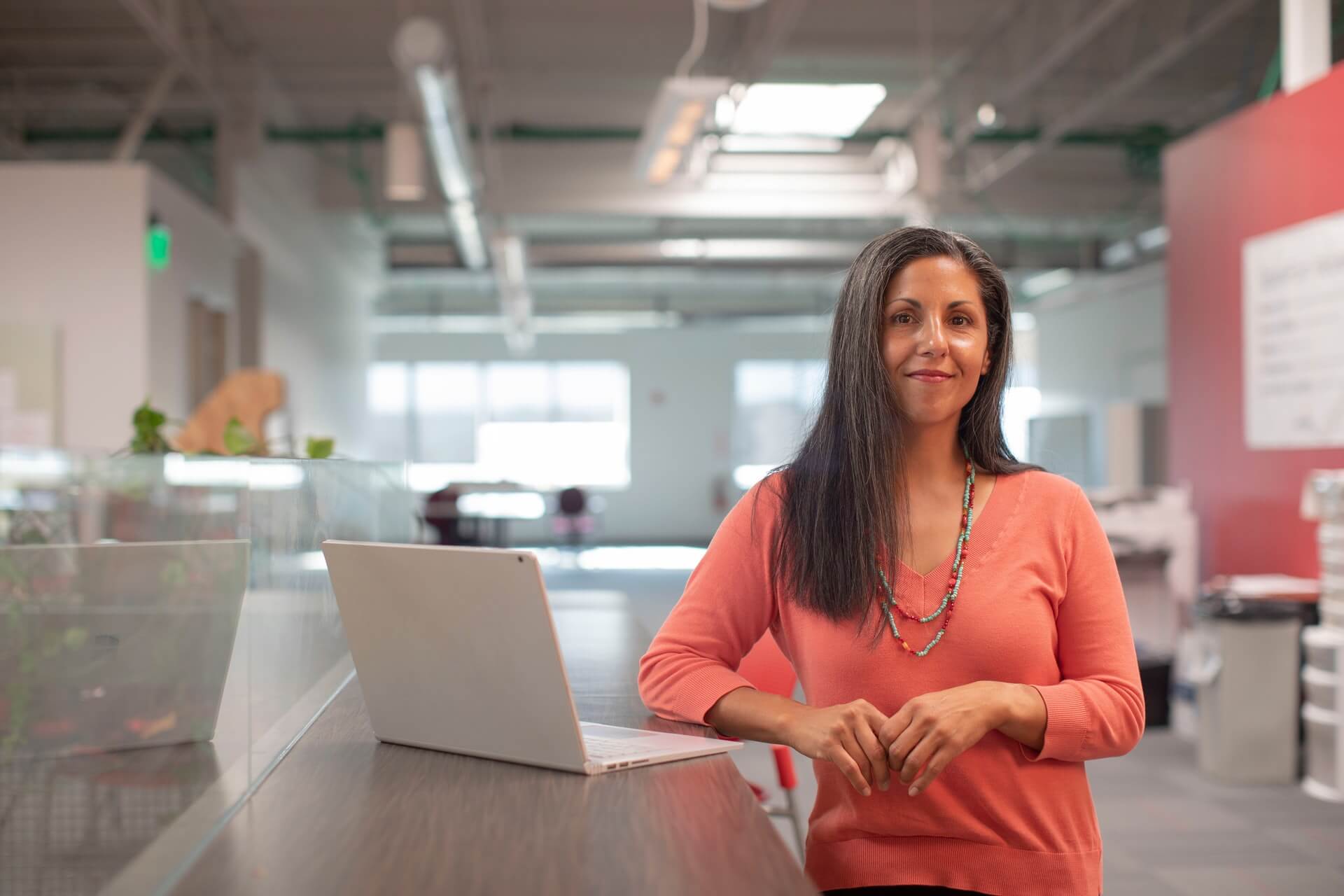 Woman standing beside a laptop on a desk in an office lobby