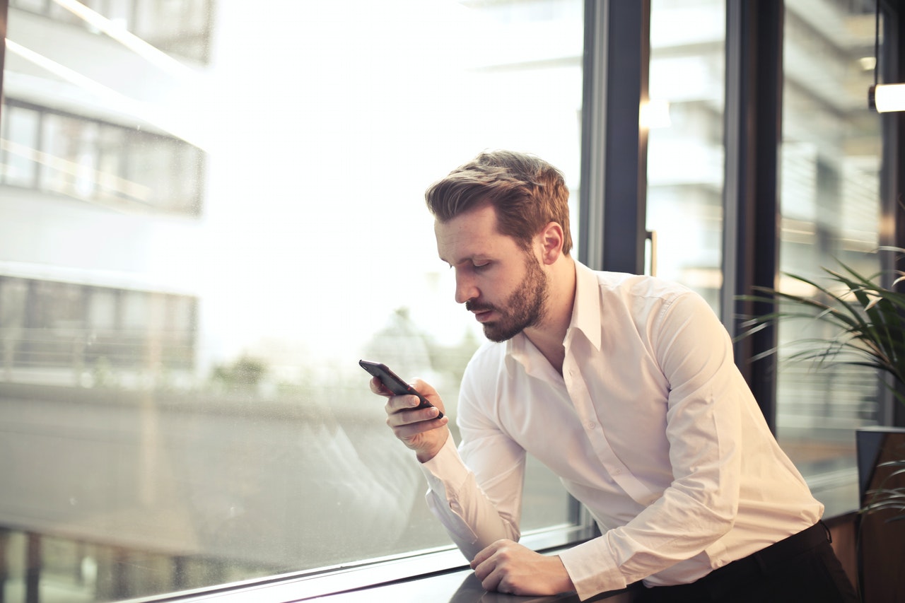 A-business-man-pressing-his-phone-beside-a-window.