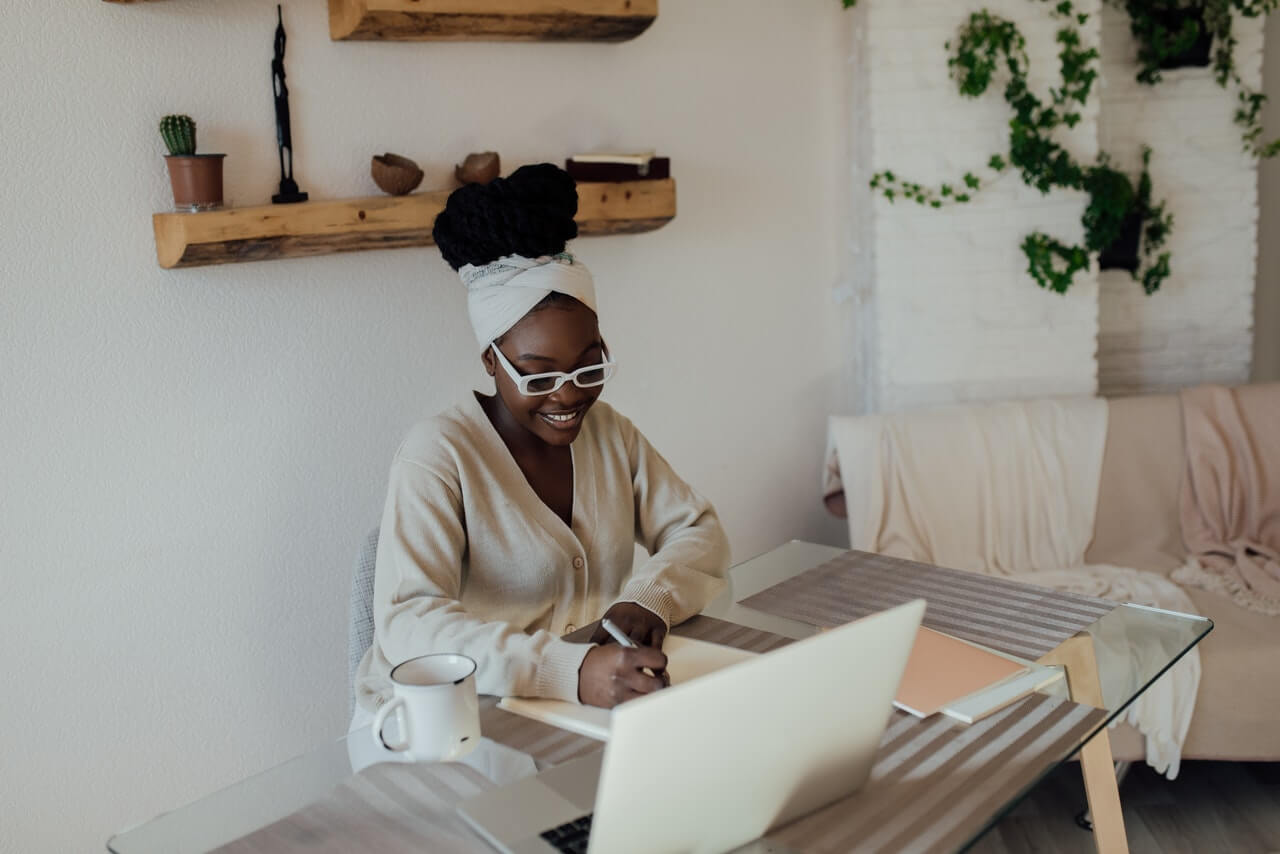 A woman writing on a paper with a laptop in front of her