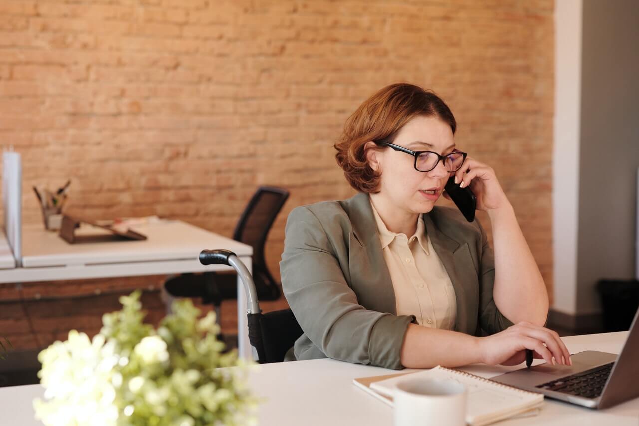 An-office-woman-having-a-conversation-with-a-phone-and-pressing-her-laptop