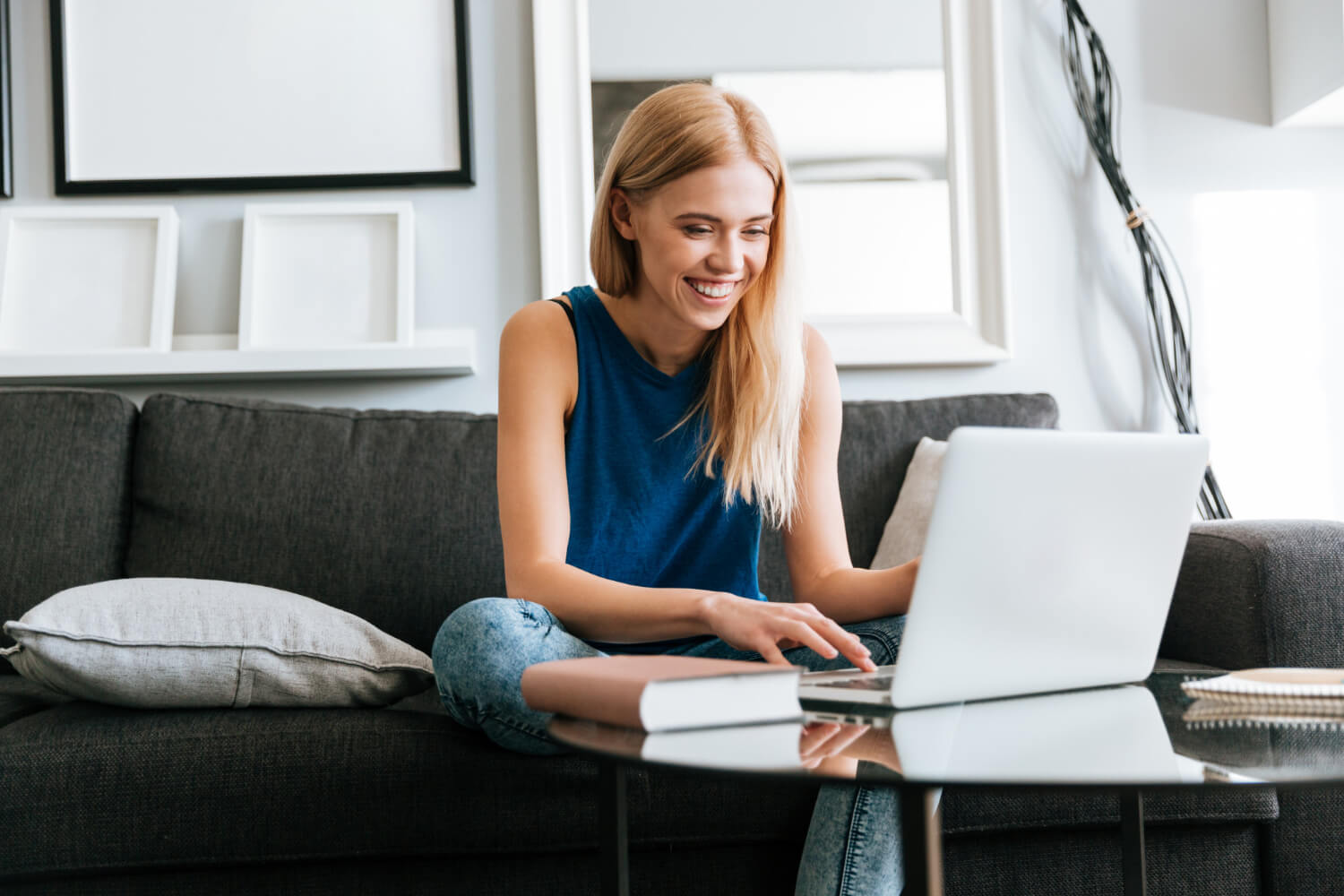 A smiling lady sitting on a sofa while working using a laptop