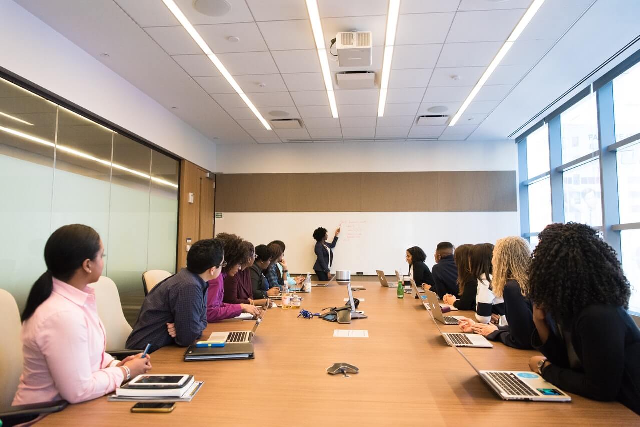 Stakeholders-in-a-meeting-hall-looking-at-a-female-speaker-writing-on-a-board