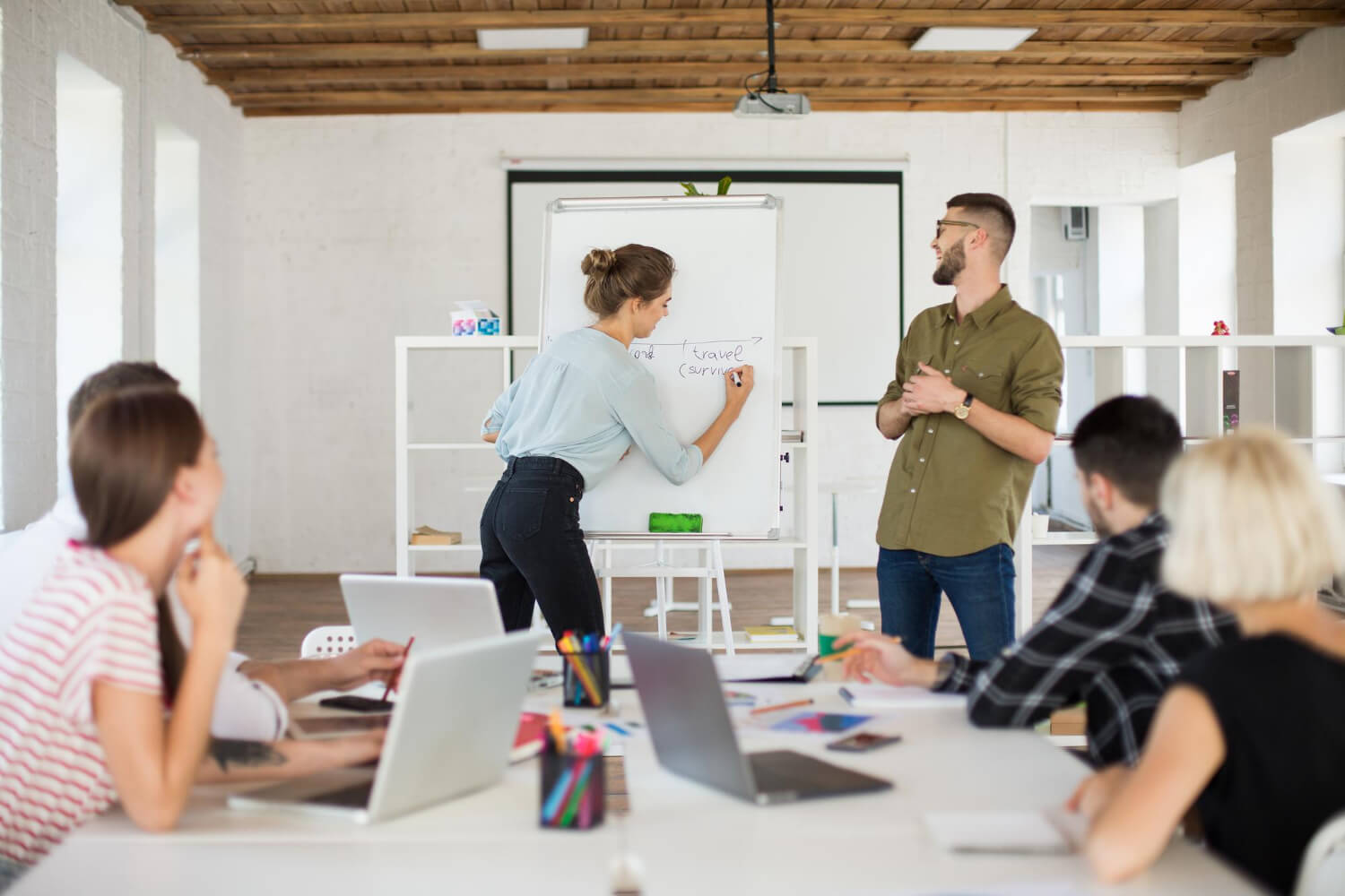 Youn woman and man presenting in an office to their colleagues