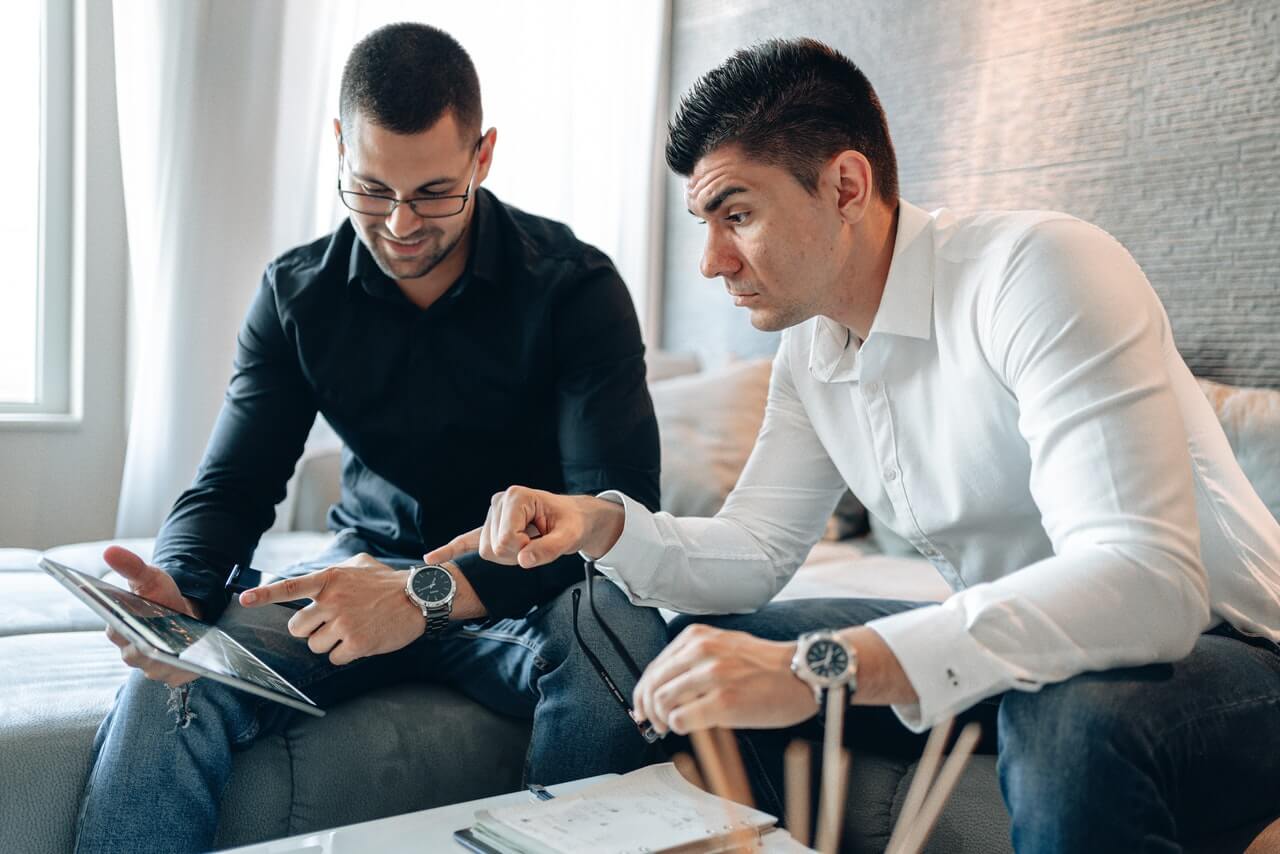 Man in Black Long Sleeve Shirt Pointing Tablet to Man in White Long Sleeve