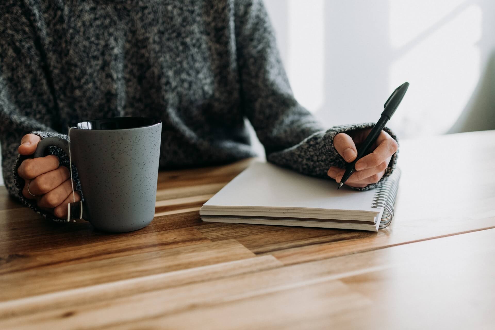 Woman holding a cup of tea, writing in a notebook