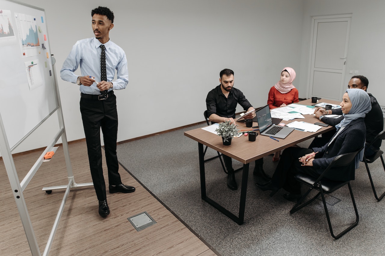 A Man Standing in Front of White Board Presenting Graphs to Colleagues