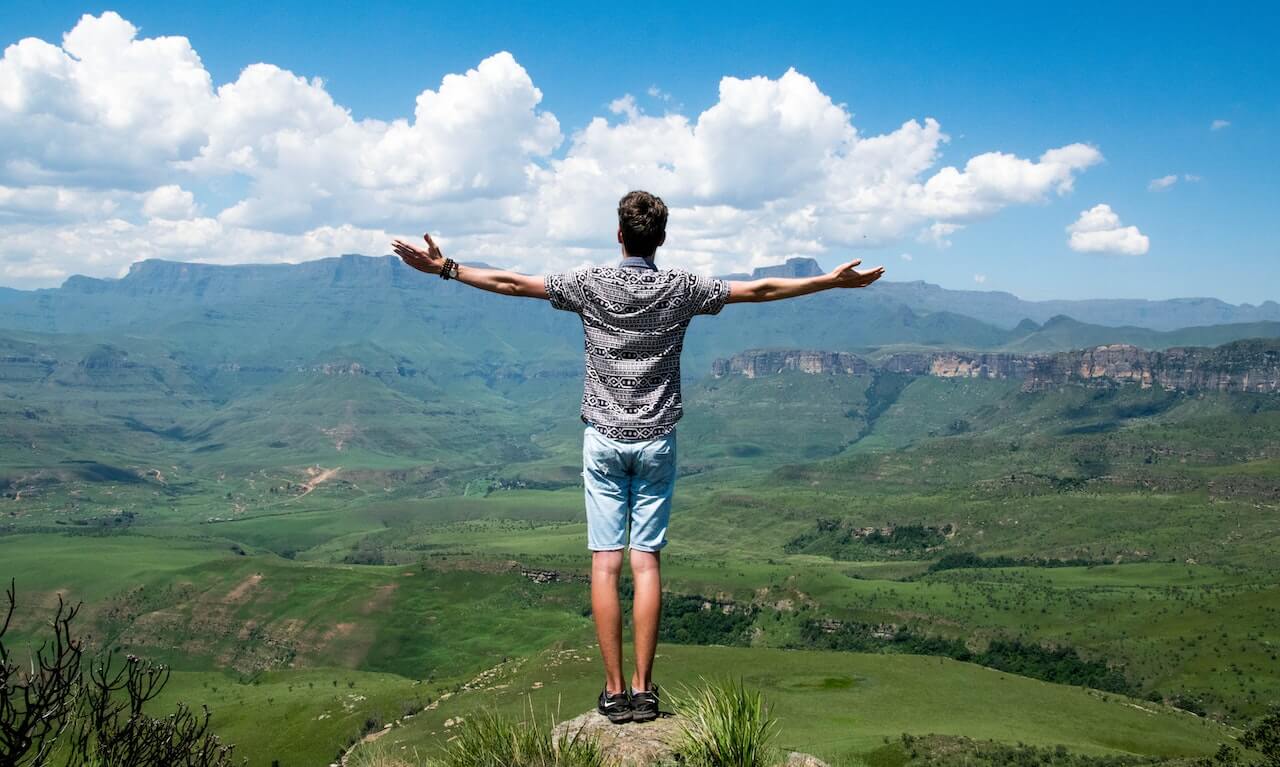 Man wearing a grey shirt standing on a rock with arms outstretched