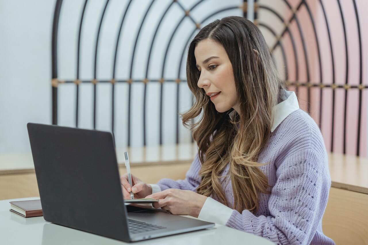 Woman writing in notebook and watching laptop