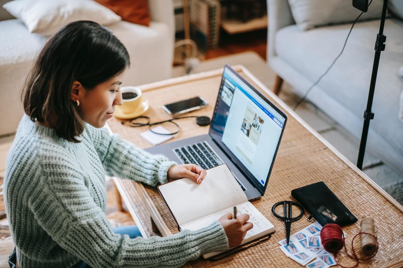 Young focused woman writing while using laptop