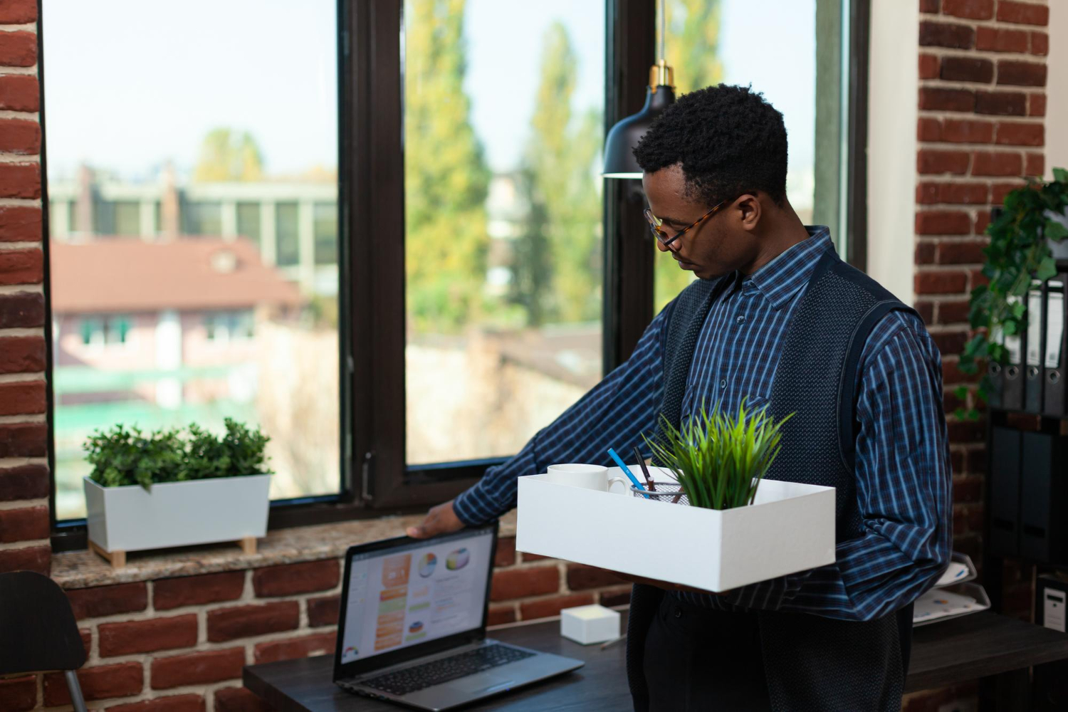 Employee-being-fired-closing-laptop-while-holding-tray-with-personal-belongings-before-leaving