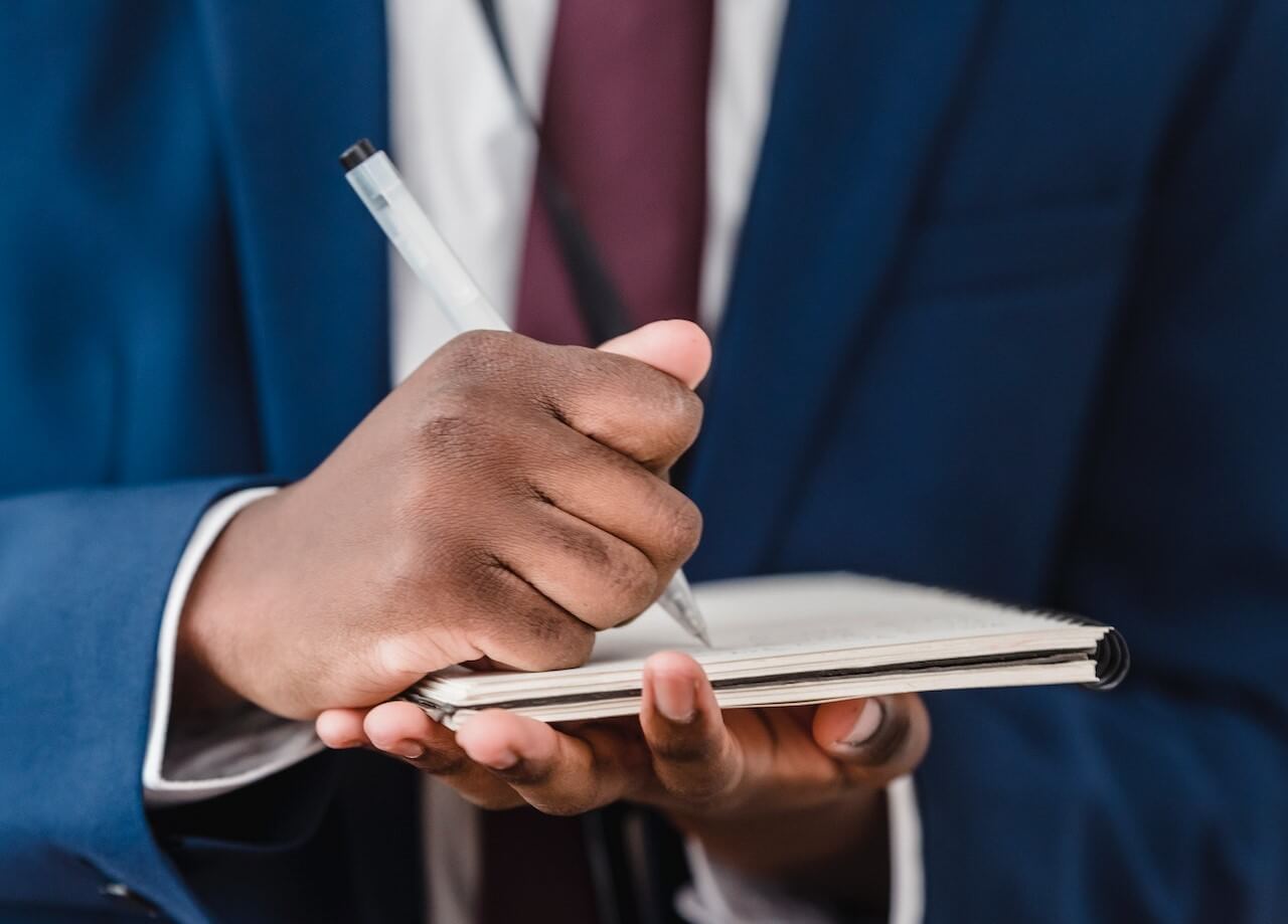 Man in Blue Suit Writing on Notebook