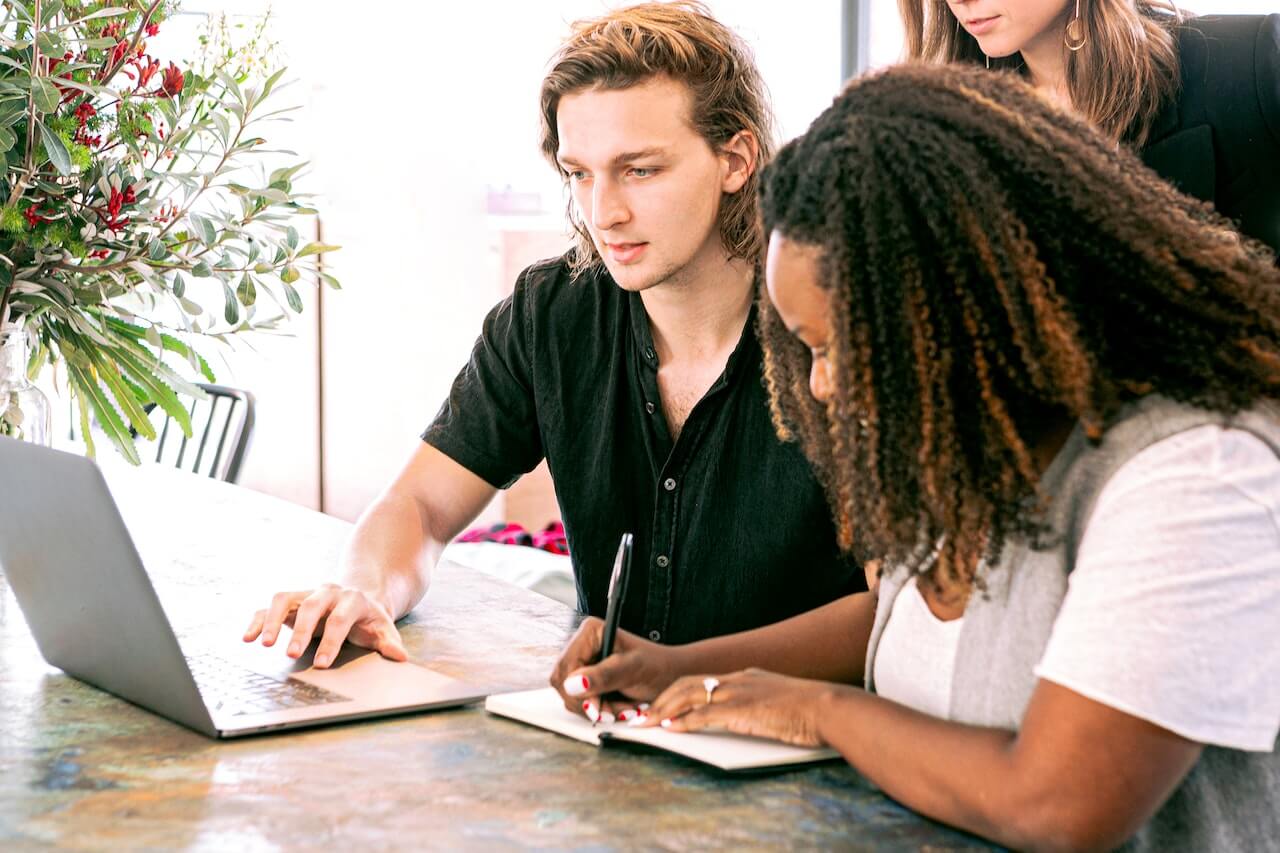 Man looking at the laptop while woman takes notes