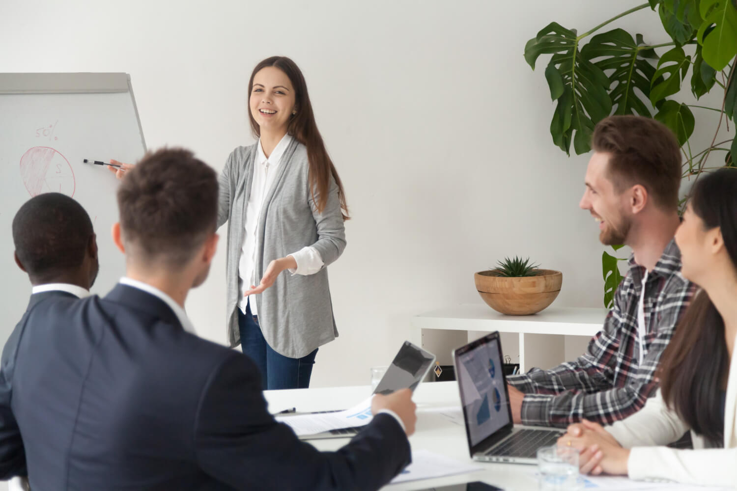 Smiling-young-employee-giving-presentation-working-with-flipchart-meeting-room