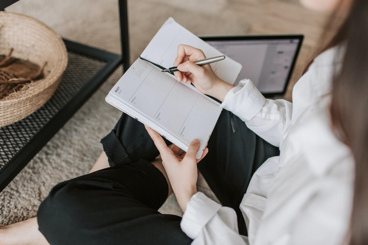 Lady sitting on the floor taking notes beside a laptop