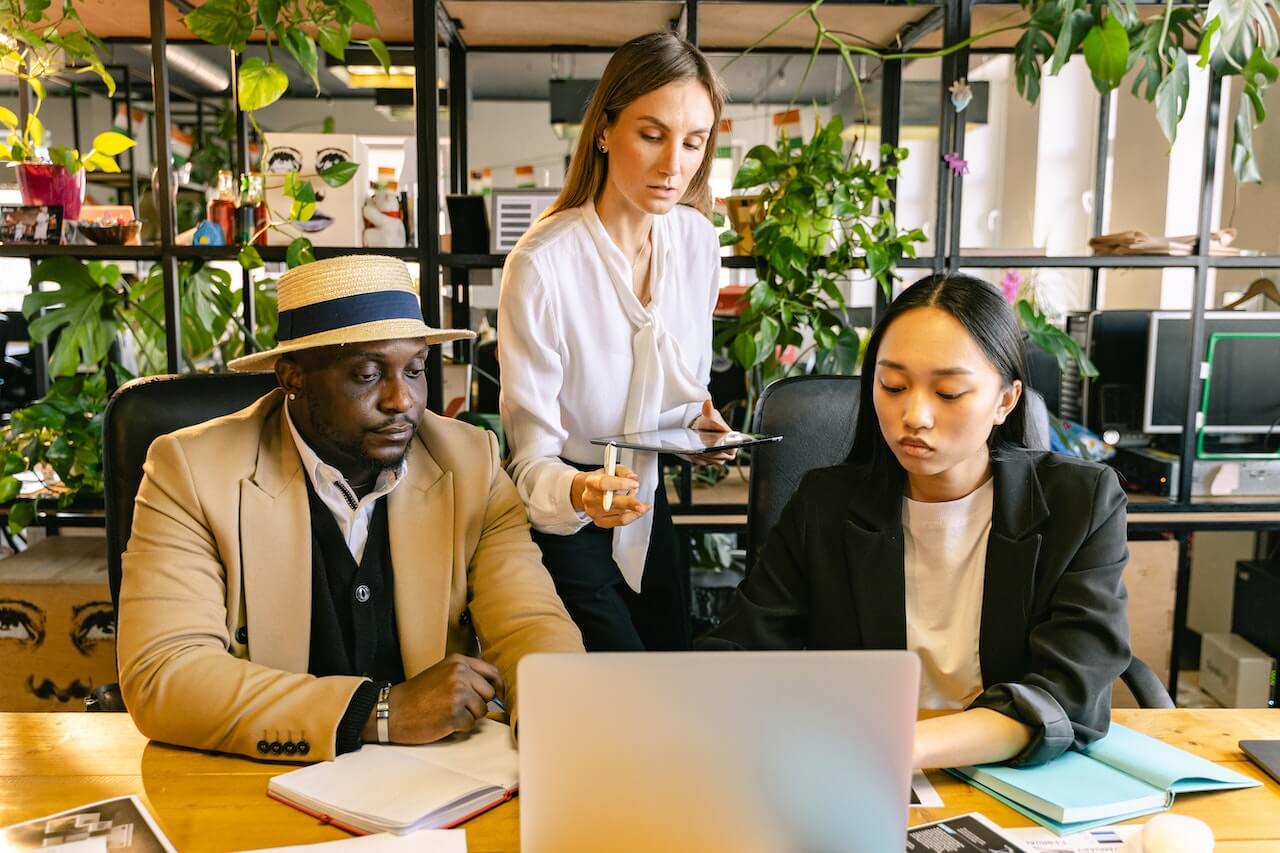 Young business woman holding a tablet looking at the laptop screen of her staff