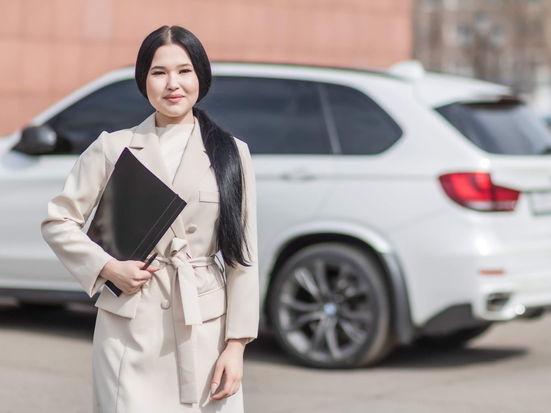 An insurance agent standing in front of a car holding a car insurance form