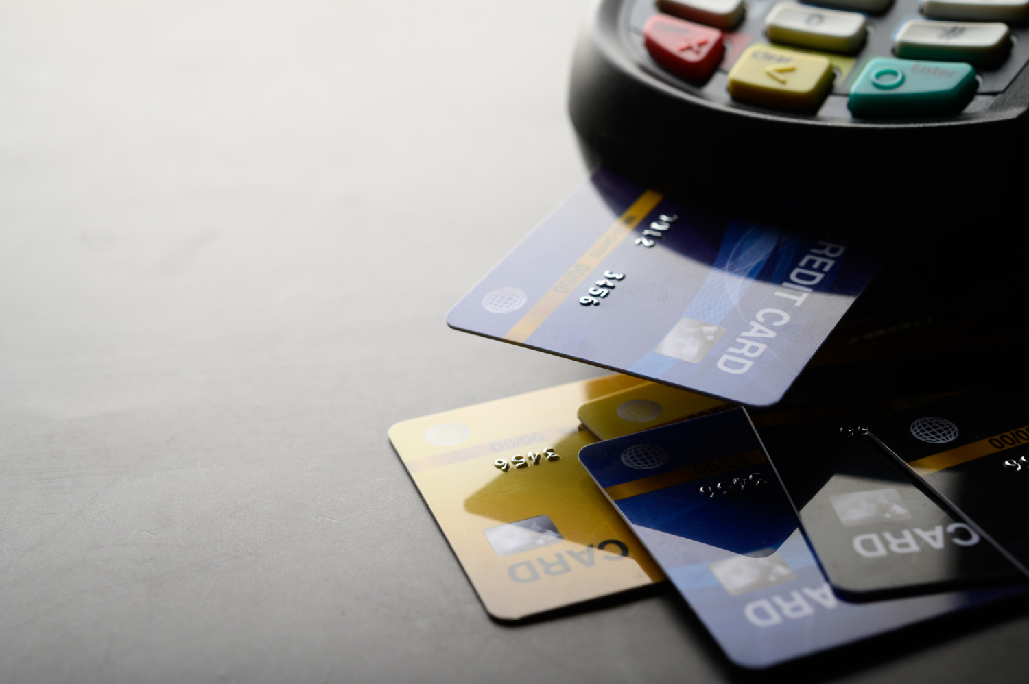 A POS machine with a bunch of debit cards on a plain surface